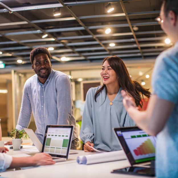 Team of employees standing around a table having a discussion with laptops open